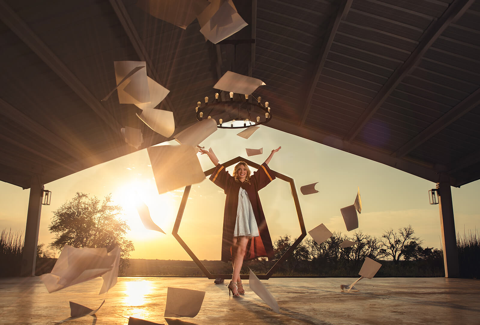 High School Senior student tossing papers at golden hour inside pavilion at Mae’s Ridge in Dripping Springs during senior photo session by Gabe Rene LLC
