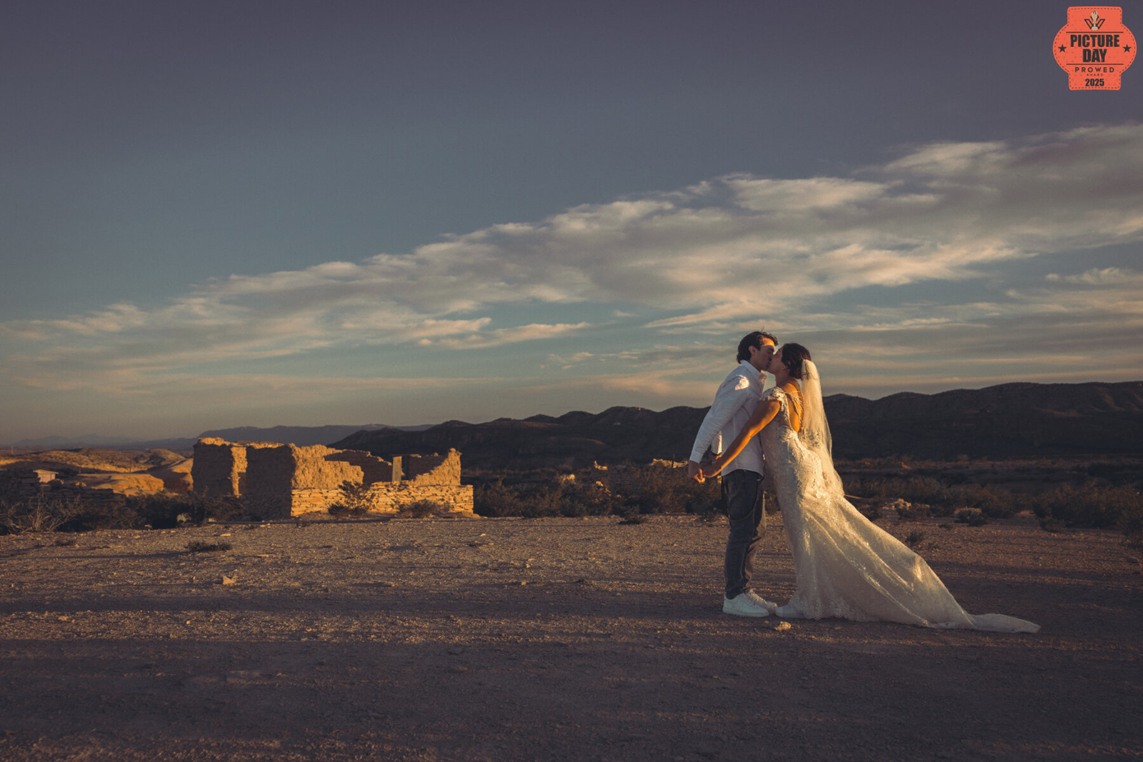 Bride and groom kiss in wedding attire at sunset among desert ruins in Terlingua, Texas during award-winning photo session by Gabe Rene LLC