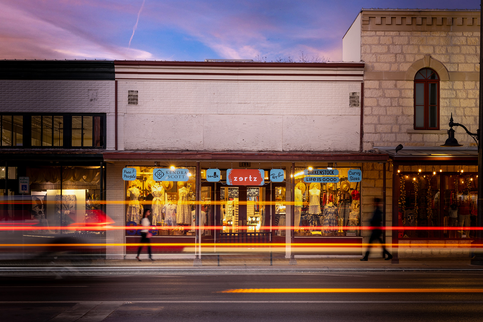 Zertz Boutique storefront at dusk with light trails and window displays featuring Kendra Scott, Free People, and Birkenstock in downtown Fredericksburg, Texas
